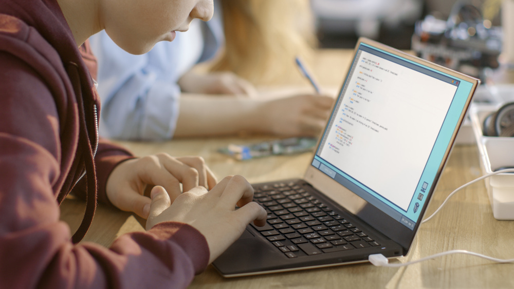 A child in brown sweater typing on a laptop.
