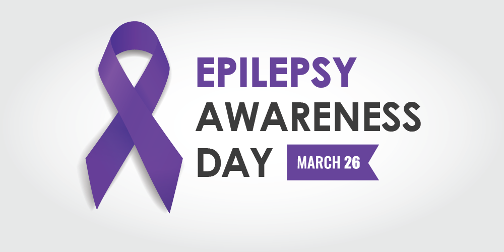 A graphic consists of a purple ribbon with Epilepsy Awareness Day March 26 written on it.