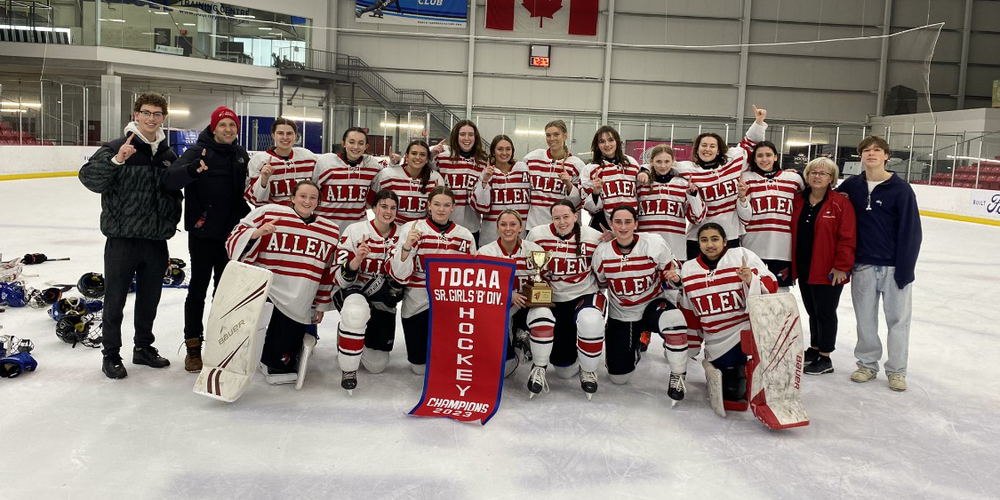 Bishop Allen Girls Hockey Team posing on the rink with their coaches and TDCAA championship banner
