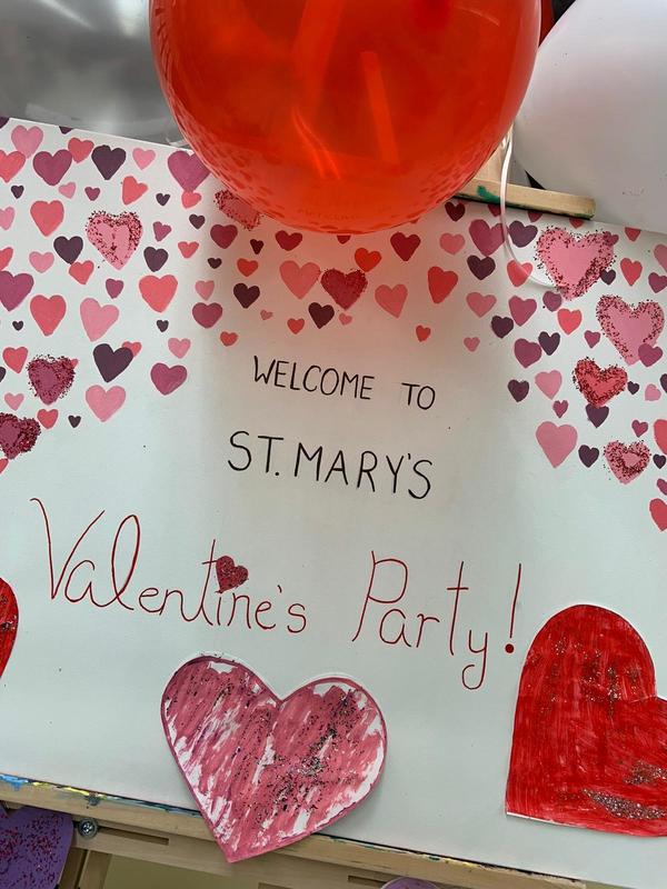 Poster saying Welcome to St. Mary's Valentine's Party with baloons around it, and the poster decorated in red and pink coloured hearts