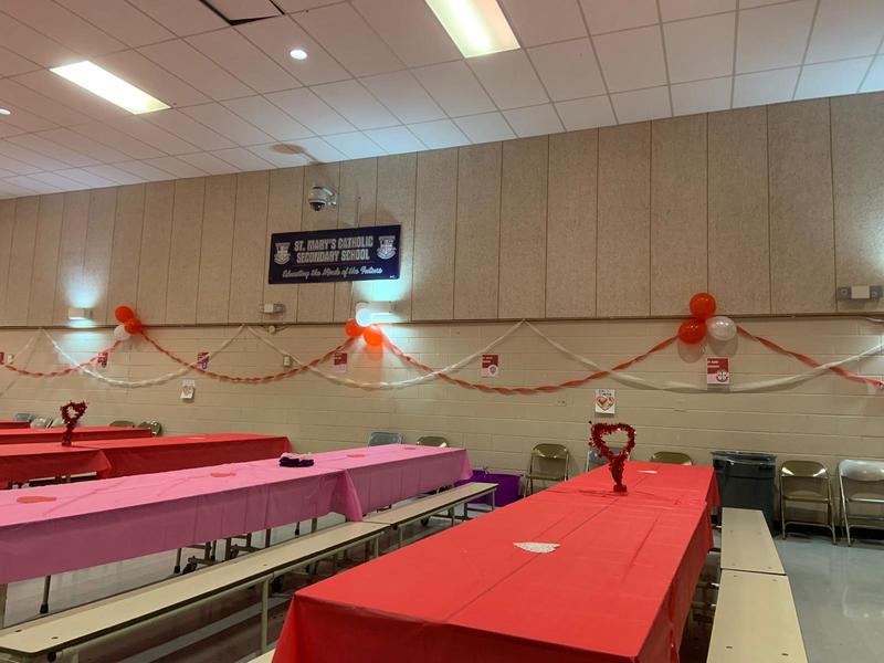 Photo of the room decorated for the party, with the tables covered in pink and red tablecloths and the walls decorated with red and white streamers and balloons
