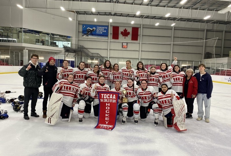 Bishop Allen Girls Hockey Team posing on the rink with their coaches and TDCAA championship banner