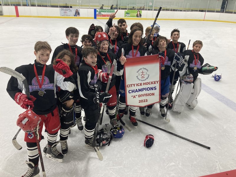 Group photo of the Our Lady of Peace Catholic School ice hockey team on the skating rink with their championship banner