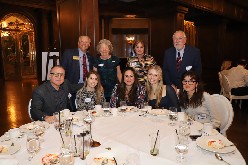 Group photo of Maya, Claudia, Jennifer, Diana, John and the Kiwanis President's Dinner hosts at a dinner table.