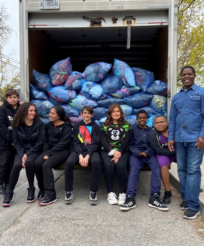 Photo of Our Lady of Victory students sitting on the back of a truck containing the bags of clothing donated, with vice principal Mr. Yeaher standing next to them.