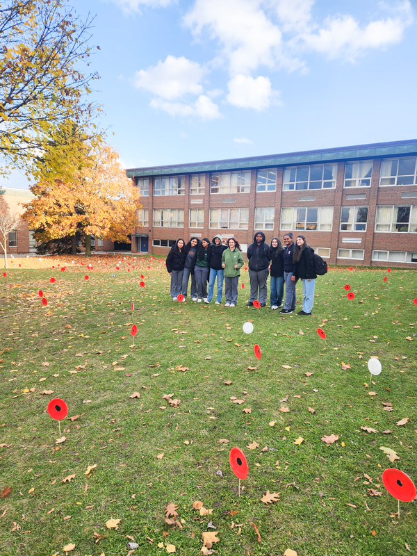 A group of Newman students stand together in the middle of the school grounds where the painted poppies have been planted