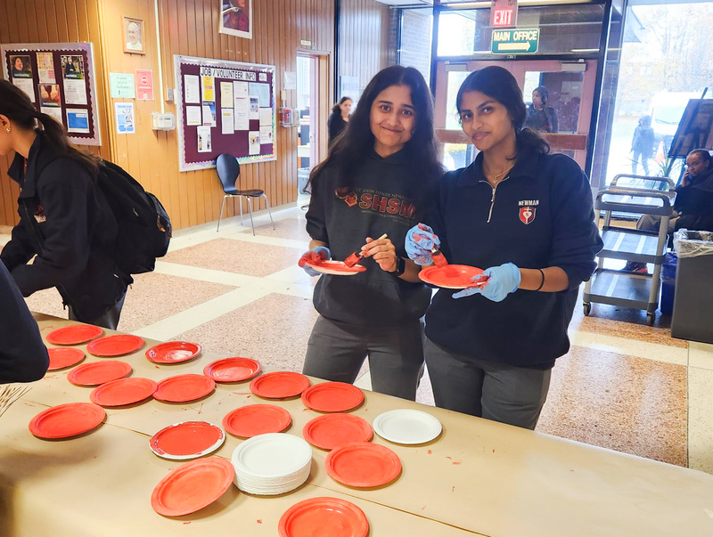 Two Newman students paint plates red and black to resemble poppies