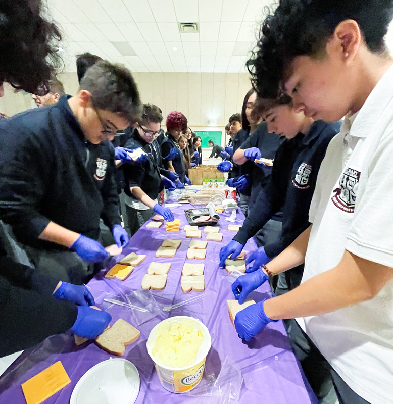 St. Mary Catholic Academy students gathered around a table wearing gloves and preparing sandwiches at Good Shepherd Ministries